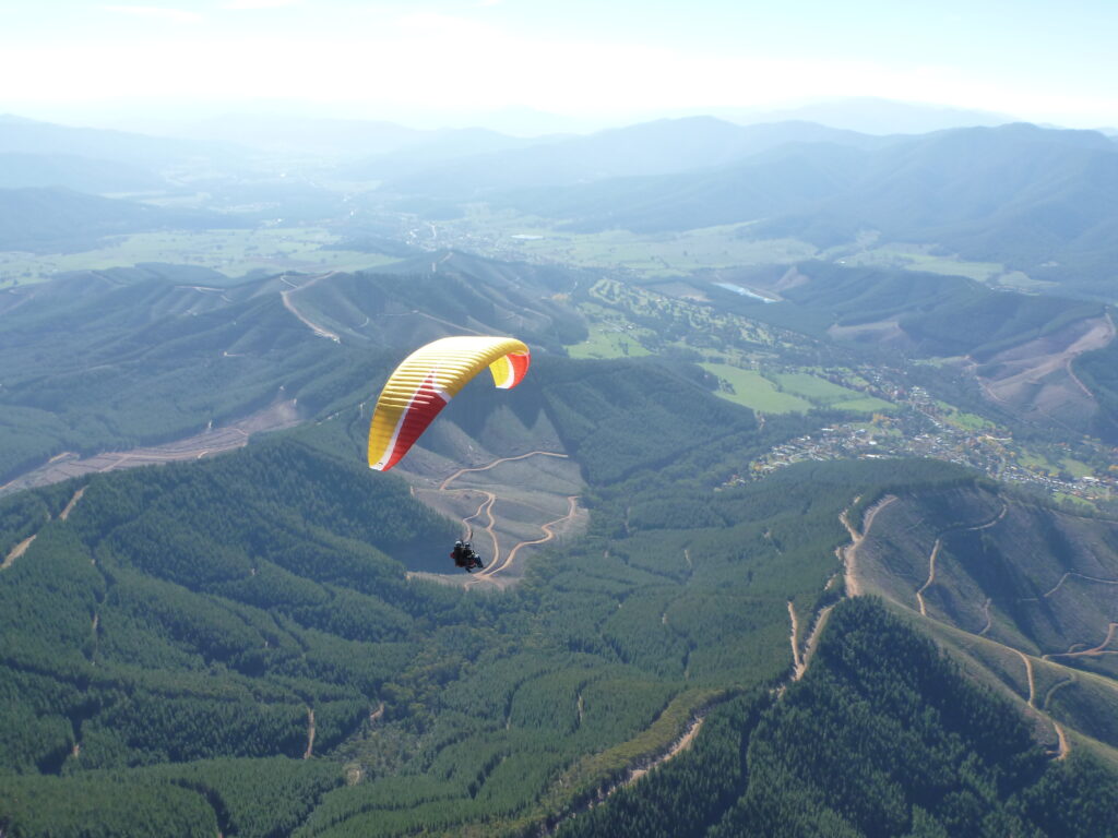 A yellow and red paraglider flies over mountains.