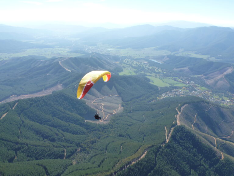 A yellow and red paraglider flies over mountains.
